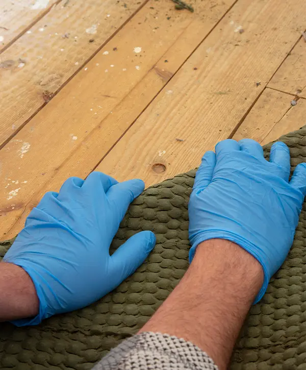 A man with blue gloves removing a carpet from an old hardwood floor