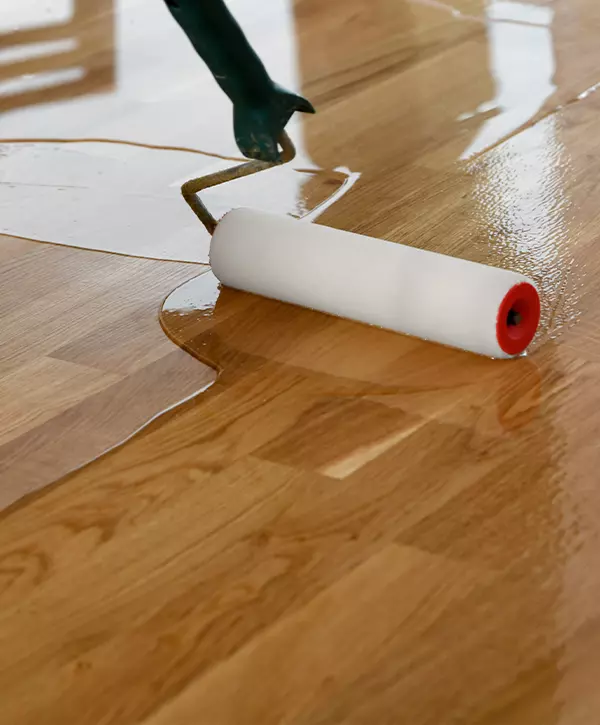 Hardwood Floor Recoating In Modesto Lacquering wood floors. Worker uses a roller to coating floors.