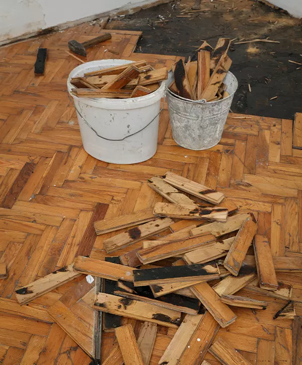 Old damaged parquet removal, heap of small planks at bitumen covered floor and buckets with wodden pieces
