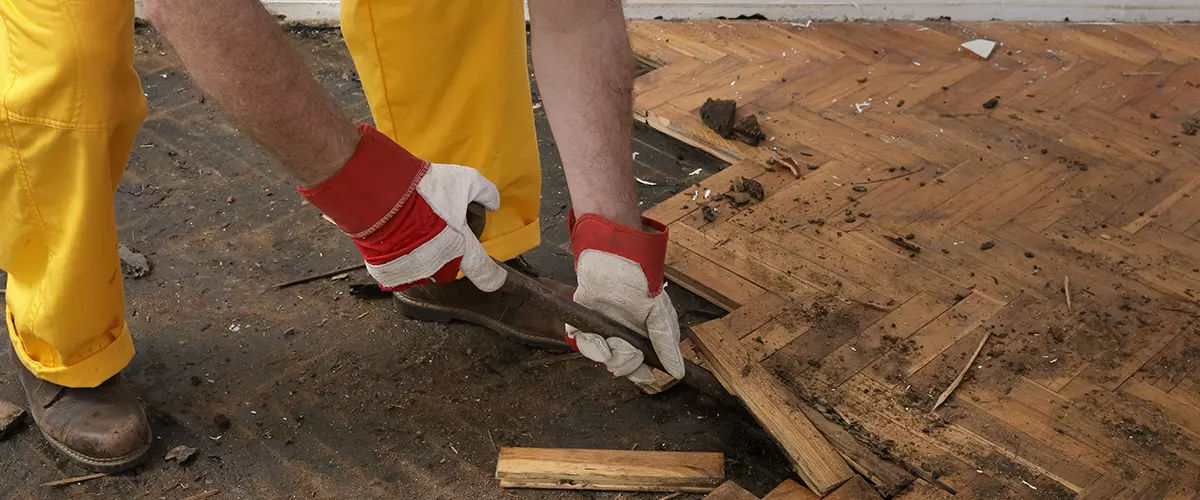 Worker removing old damaged parquet using crowbar tool