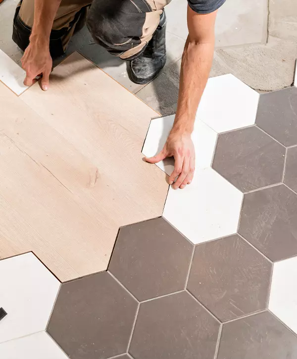 Male worker installing new wooden laminate flooring. The combination of wood panels of laminate and ceramic tiles in the form of honeycomb. Kitchen flooring installation